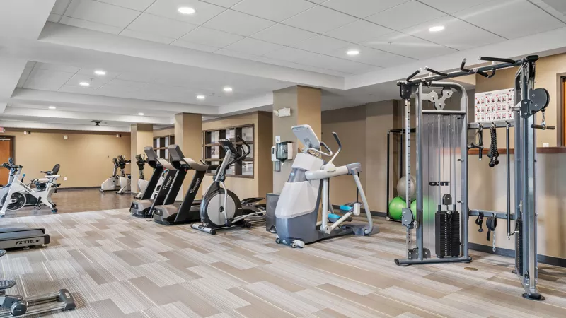Empty fitness center with multiple treadmills, elliptical trainers, stationary bikes, and a multi-station weight machine.