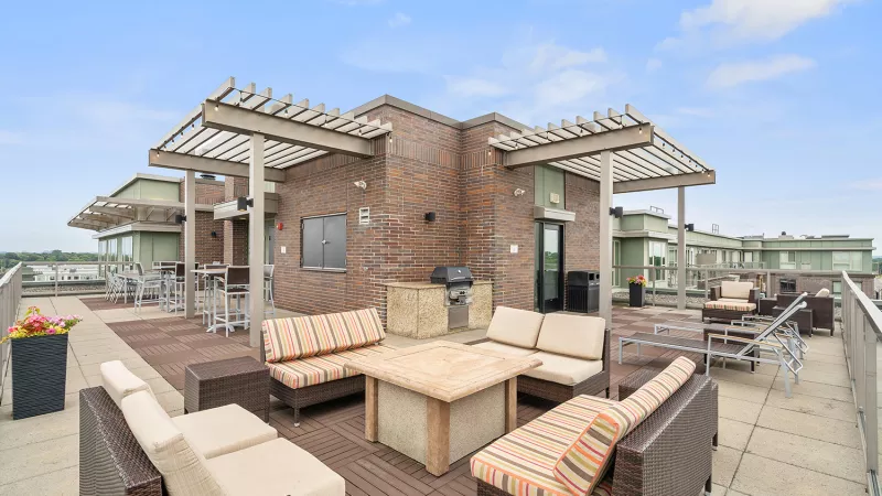 Spacious rooftop patio featuring outdoor lounge sofas, fire pit table, barbecue grill, and shaded pergolas.