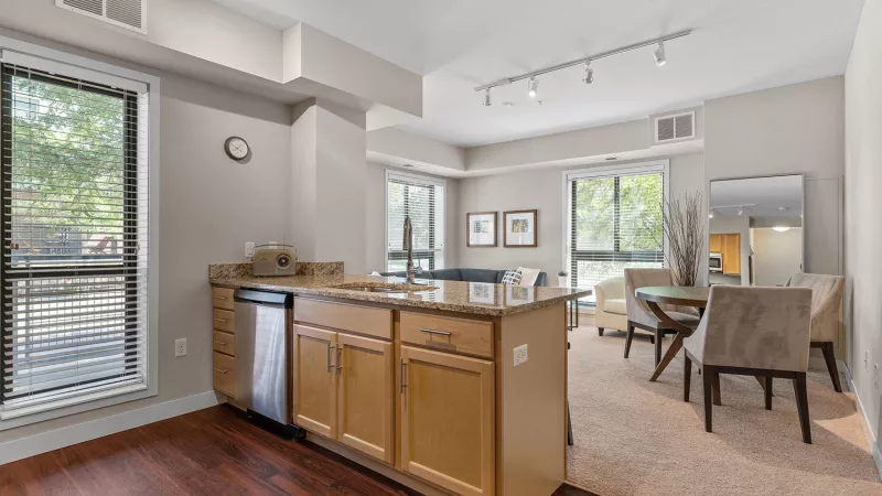 Modern open-concept kitchen with light wood island and dark wood floor, flowing into a carpeted dining area with a round table.
