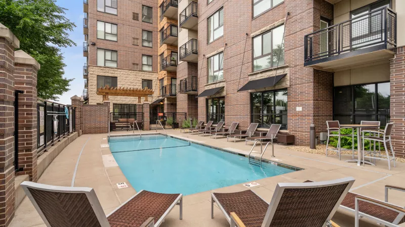 Outdoor swimming pool with lounge chairs and tables, set against a modern apartment building.