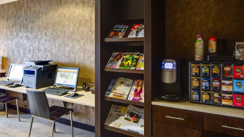 Business center with two computers, a printer, a magazine rack, and a self-serve coffee station.