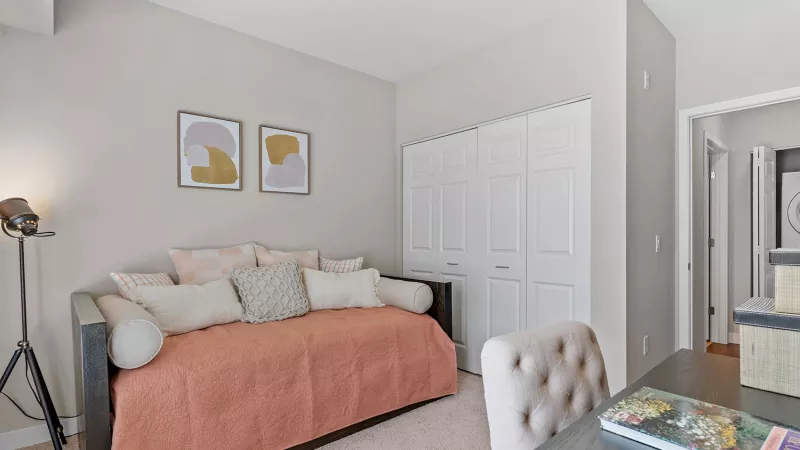 Bright room with a daybed, coral throw, abstract art, desk with a chair, and a camera on a tripod.