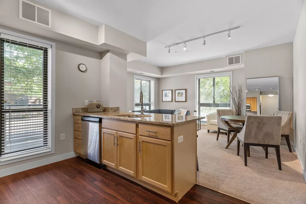 Modern open-concept kitchen with light wood island and dark wood floor, flowing into a carpeted dining area with a round table.